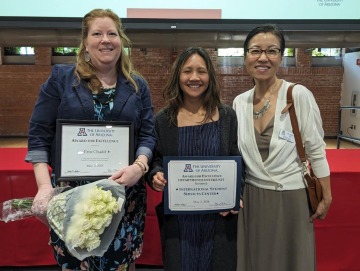 Three individuals pose with two of the individuals holding up certificates